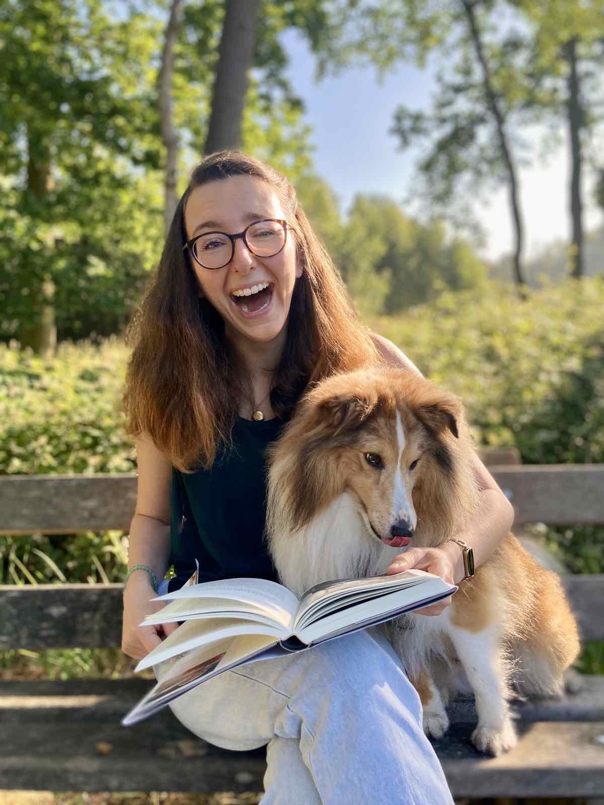 Annelies leest lachend een boek met haar sheltie naast zich